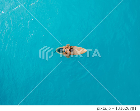 Surf girl sitting on surfboard in blue ocean. Aerial view 131626781