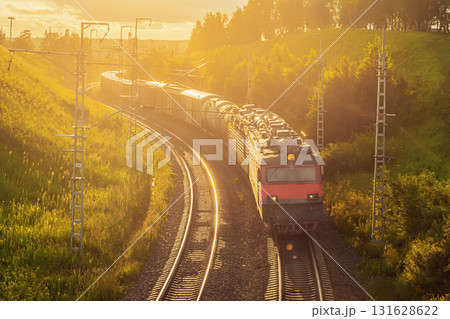 A freight train, comprised of a powerful locomotive and various freight wagons including oil tanks, gracefully navigates a winding railway track. A freight train, comprised of a powerful locomotive and various freight wagons including oil tanks, gracefully navigates a winding railway track. 131628622