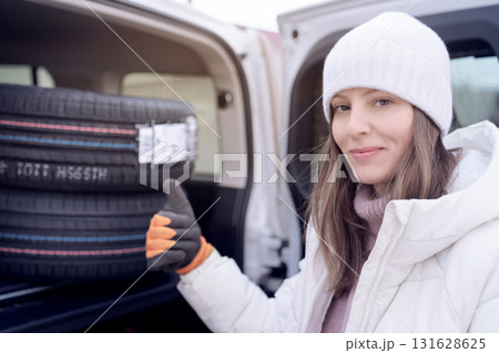 Happy woman loads new tires into her car trunk for seasonal tire change in winter. purchase and sale of new tires for the season. Happy woman loads new tires into her car trunk for seasonal tire change in winter. purchase and sale of new tires for the season. 131628625