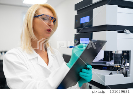 Professional blonde scientist writing a report on HPLC data. Pharmaceutical science and testing. 131629681