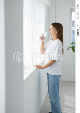 窓辺で自然光を浴びながらペットボトルの水を手に持つ日本人女性 131630260