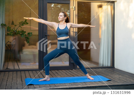 Young woman doing yoga and standing a warrior pose Young woman doing yoga and standing a warrior pose 131631996