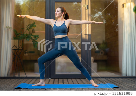 Young woman doing yoga and standing a warrior pose Young woman doing yoga and standing a warrior pose 131631999