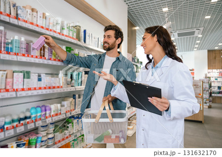 Healthcare professional giving advice to man with shopping basket inside drugstore 131632170