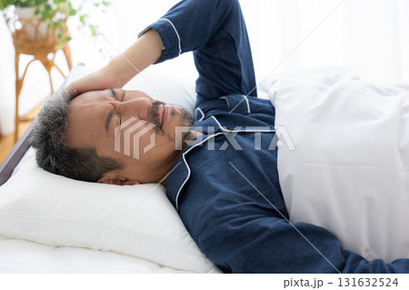 ベッドで頭をおさえるミドル男性 ベッドで頭をおさえるミドル男性 131632524
