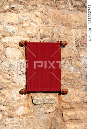 Decorative fabric scroll on a medieval stone wall. Old red textile scroll with rolled edges. Unique, vintage look, adding a touch of history to project. Copy space for text 131632761