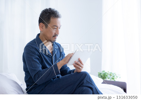 ベッドでタブレットを見るミドル男性 131633050