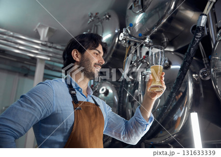 A man is holding a glass of beer while inside a brewery setting A man is holding a glass of beer while inside a brewery setting 131633339