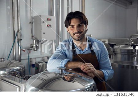 A man wearing an apron is leaning against a large metal container 131633340
