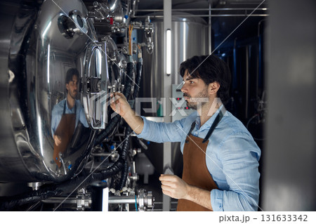A man in an apron stands confidently in a factory, arms crossed A man in an apron stands confidently in a factory, arms crossed 131633342