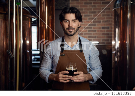A man wearing an apron is holding a frosty glass of beer A man wearing an apron is holding a frosty glass of beer 131633353