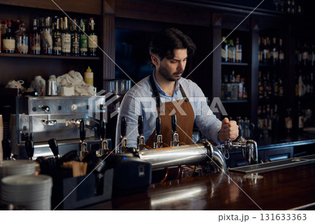 Handsome brewer is standing behind a bar counter, serving customers 131633363