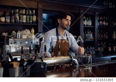 Handsome brewer is standing behind a bar counter, serving customers Handsome brewer is standing behind a bar counter, serving customers 131633364