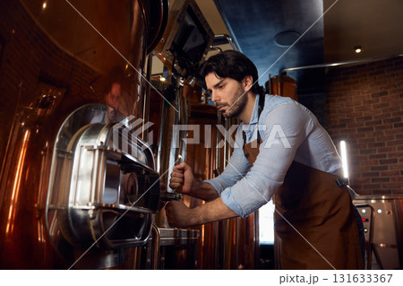 A man wearing an apron is diligently working on a complex machine A man wearing an apron is diligently working on a complex machine 131633367