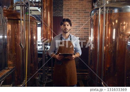 Confident man in an apron is holding a digital tablet inside a brewery 131633369