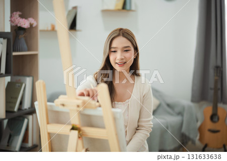 Young woman smiling while painting on canvas in cozy room with bright natural light, creative hobby, artistic expression, living space inspiration Young woman smiling while painting on canvas in cozy room with bright natural light, creative hobby, artistic expression, living space inspiration 131633638