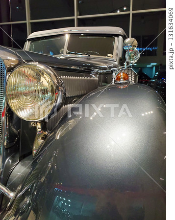 Vintage classic car with polished chrome details, round headlights, and glossy metallic paint, displayed indoors under artificial lighting. Craftsmanship and timeless design of antique automobile 131634069
