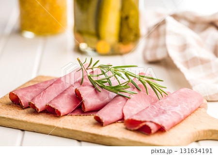 Sliced beef pastrami on cutting board on white table. 131634191