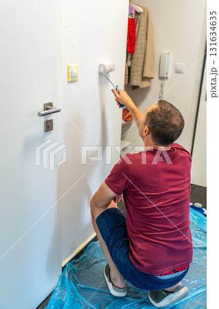 Man painting the wall with a roller in white during home renovation. Interior improvement, surface transformation and DIY work with paint tools. Man painting the wall with a roller in white during home renovation. Interior improvement, surface transformation and DIY work with paint tools. 131634635