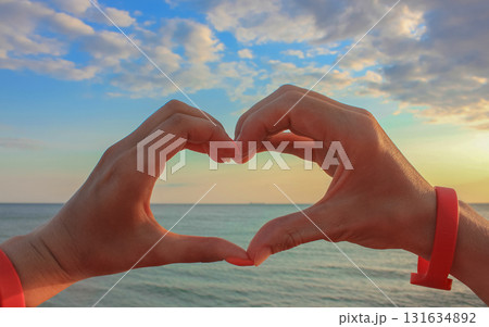 The hands of woman and man in the form of hearts over blue skies, clouds and sea. Hands in the form of love hearts - love concept. The hands of woman and man in the form of hearts over blue skies, clouds and sea. Hands in the form of love hearts - love concept. 131634892