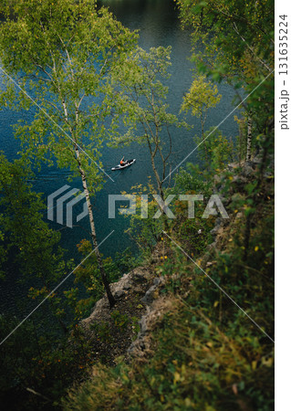 Kayaker gliding across serene lake, framed by birch trees atop cliff, embracing tranquility and beauty of nature in picturesque outdoor landscape. Kayaker navigating calm lake waters. Natural beauty Kayaker gliding across serene lake, framed by birch trees atop cliff, embracing tranquility and beauty of nature in picturesque outdoor landscape. Kayaker navigating calm lake waters. Natural beauty 131635224