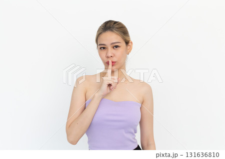 Beautiful Asian woman silently gestures to the camera, putting her finger on her lips, revealing her beauty secret, demonstrating her skincare routine, on white background. Beautiful Asian woman silently gestures to the camera, putting her finger on her lips, revealing her beauty secret, demonstrating her skincare routine, on white background. 131636810