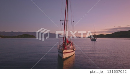 Two sailboats floating on calm ocean water bay during vibrant sunset and silhouetted hills. Travel, tourism, holiday, relax, active lifestyle Amazing nature landscape, remote destination. Drone flight 131637032