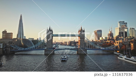 England, London: Aerial view tourist boat sailing River Thames under Tower Bridge, with The Shard and City of London skyline in the background during a beautiful bright sunset. Drone flight England, London: Aerial view tourist boat sailing River Thames under Tower Bridge, with The Shard and City of London skyline in the background during a beautiful bright sunset. Drone flight 131637036