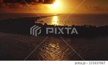 French Polynesia, Rangiroa island: Golden sunset illuminating Tiputa Pass in Rangiroa, French Polynesia, with sailboats moored in calm lagoon waters. Wild nature travel landscape. Drone flight 131637067