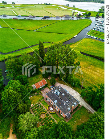 Aerial view of eco conscious estate with solar paneled roof, red roofed annex, formal garden, pond, and outdoor patio nestled in lush greenery with parked cars and dirt path access. Aerial view of eco conscious estate with solar paneled roof, red roofed annex, formal garden, pond, and outdoor patio nestled in lush greenery with parked cars and dirt path access. 131637628