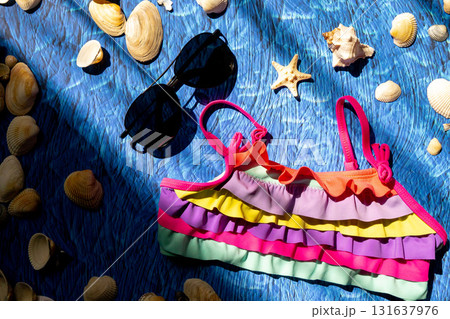 A collection of travel items including suitcase, sunglasses, swim suit, sunscreen and shells on turquoise navy blue background A collection of travel items including suitcase, sunglasses, swim suit, sunscreen and shells on turquoise navy blue background 131637976
