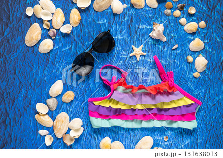 A collection of travel items including suitcase, sunglasses, swim suit, sunscreen and shells on turquoise navy blue background 131638013