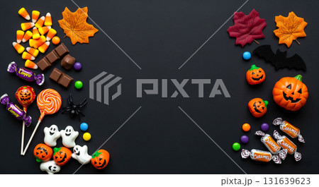 Halloween Candy Background Concept with assorted sweets and spooky decorations on black table, flat lay top view with copy space for party invitation text 131639623