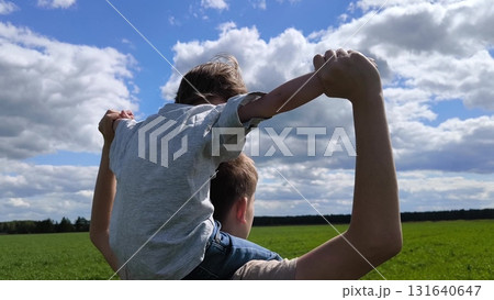 Son is on brother's shoulders with his arms outstretched. rear view. Boy sitting on dads shoulders. Happy family. Family vacation, travel in summer. concept of a happy childhood Son is on brother's shoulders with his arms outstretched. rear view. Boy sitting on dads shoulders. Happy family. Family vacation, travel in summer. concept of a happy childhood 131640647