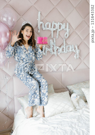 Woman celebrating birthday holding pink cake with balloons and happy birthday sign Woman celebrating birthday holding pink cake with balloons and happy birthday sign 131643382