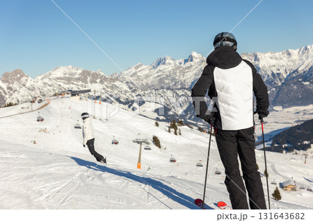 Back view skier standing on snowy slope overlooking Austrian Alps under clear blue sky. Bright winter day filled with crisp air, panoramic mountain views, and peaceful alpine adventure atmosphere 131643682