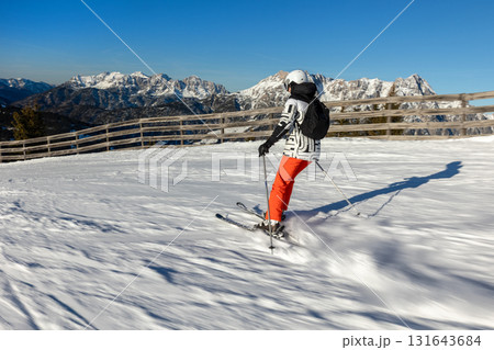 Young adult confident woman skier skiing fast downhill winter alpine skiing resort. Female sporty person with backpack mountain Alps snow slope outdoors cold snowy sunny backlit light day 131643684