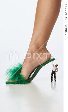 Bold colorful poster. Tiny man supporting giant green heel in surreal fashion power scene Bold colorful poster. Tiny man supporting giant green heel in surreal fashion power scene 131644355