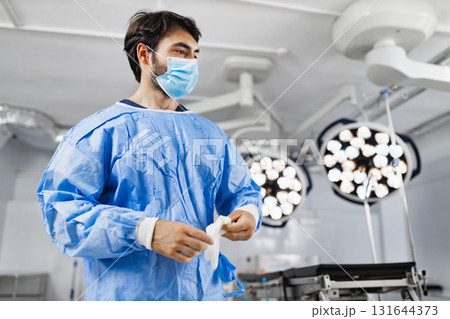 A surgeon wearing a mask and surgical gown prepares for an operation in a modern operating room. 131644373