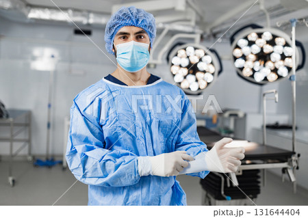 A surgeon wearing a mask and surgical gown prepares for an operation in a modern operating room. 131644404