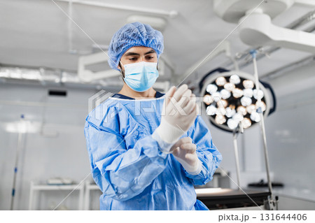 A surgeon is putting on gloves in a sterile operating room, preparing for a medical procedure. 131644406