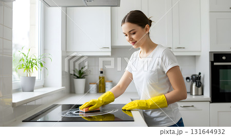 Female in yellow rubber gloves is actively cleaning kitchen countertop and stove with sponge, surrounded by modern house featuring natural light, minimalistic decor, creating fresh, inviting ambiance 131644932