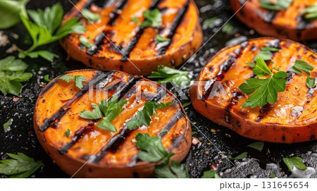 Grilled sweet potato slices garnished with fresh herbs on a black background, seasoned with salt and spices. A healthy and flavorful dish perfect for festive meals or holiday gatherings Grilled sweet potato slices garnished with fresh herbs on a black background, seasoned with salt and spices. A healthy and flavorful dish perfect for festive meals or holiday gatherings 131645654