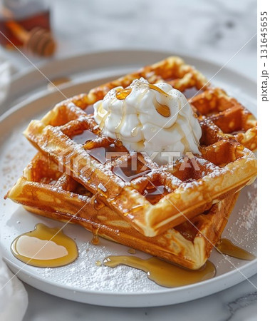 Stack of golden waffles topped with whipped cream and maple syrup, served on a white plate. A sweet and cozy breakfast perfect for holidays, brunch, or weekend mornings 131645655