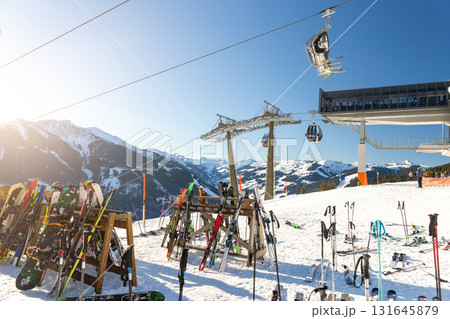 Sunny winter day on alpine slope with skis and snowboards resting near gondola station. Bright sunlight, blue sky, and mountain panorama create atmosphere of adventure, freedom, and relaxation Sunny winter day on alpine slope with skis and snowboards resting near gondola station. Bright sunlight, blue sky, and mountain panorama create atmosphere of adventure, freedom, and relaxation 131645879
