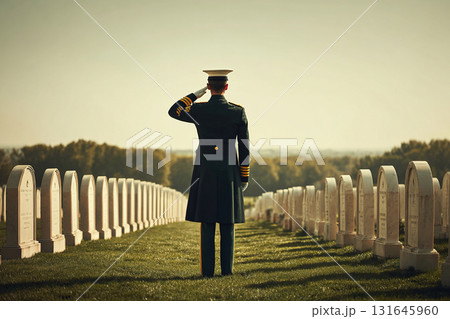 A military officer salutes in a cemetery among tombstones. White tombstones and green grass. 131645960