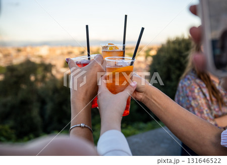 Female hands holding colorful cocktails with orange slice and straw during outdoor celebration Female hands holding colorful cocktails with orange slice and straw during outdoor celebration 131646522