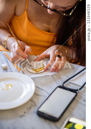 Woman painting small round canvas with fine brush at table 131646529