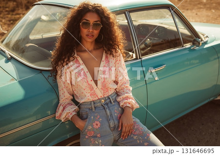 Retro model in flared denim leans casually beside turquoise vintage car 131646695