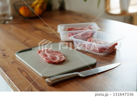 Raw pork steak on cutting board with knife and packaged meat in kitchen 131647336